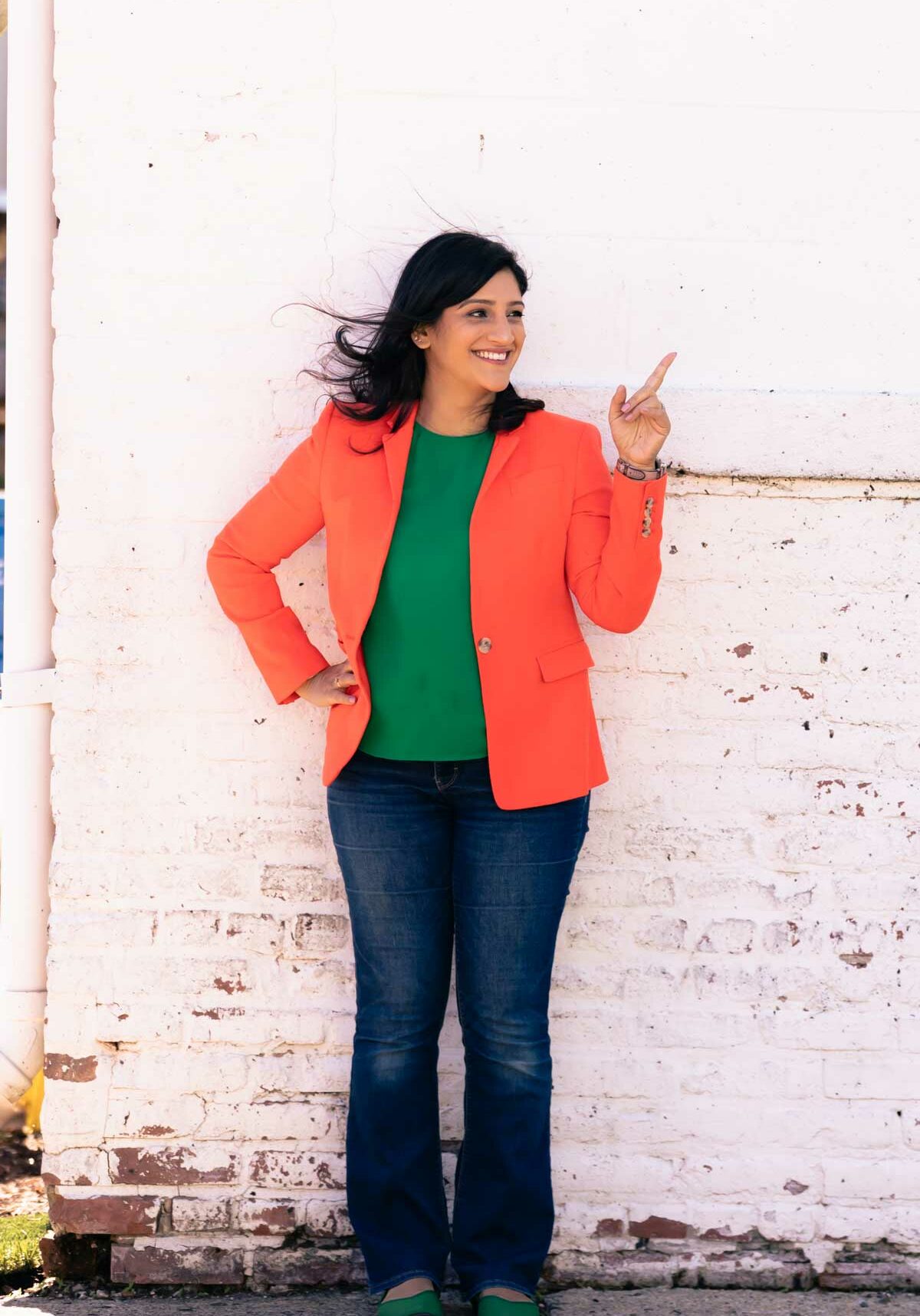 Ruchi Kaul MD, a doctor in an orange blazer and green shirt, pointing over her right shoulder while smiling